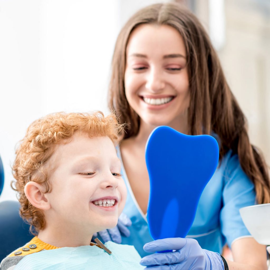 A pediatric dentist showing a young patient their smile via mirror
