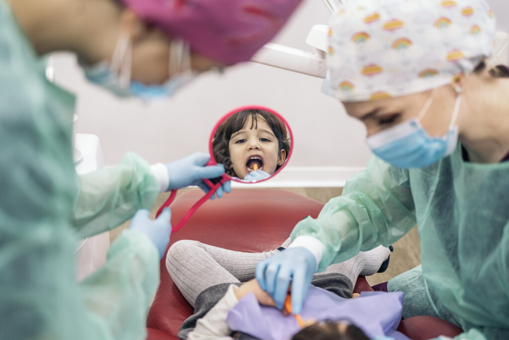 Stock photo of young girl in the dental clinic learning how to clean her teeth with a mirror.